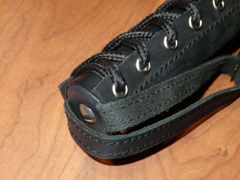 May include: Close-up of a black leather object with a lace-up design and silver eyelets. The object has a strap and is stitched with black thread. The leather appears to be textured.