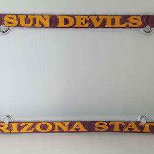 May include: A chrome license plate frame with maroon and gold accents. The top band reads "SUN DEVILS" in gold lettering. The bottom band reads "ARIZONA STATE" in gold lettering.