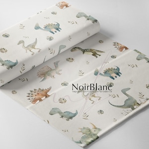 May include: White fabric roll with a repeating pattern of watercolor dinosaurs in shades of blue, brown, and green, along with leaf accents. The fabric is printed with the text "NoirBlanc impression textile broderie."