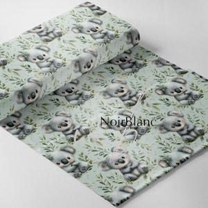 May include: A roll of fabric featuring a repeating pattern of watercolor koala bears and green foliage on a light green background. The fabric has a soft, inviting aesthetic, perfect for children's projects. The text "NoirBlanc" is visible.