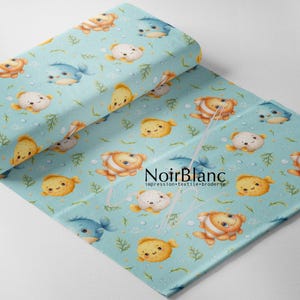 May include: A light blue fabric featuring a repeating pattern of cartoon fish in orange, yellow, and blue, along with green seaweed and white bubbles. The text NoirBlanc impression textile broderie is printed in black in the center.