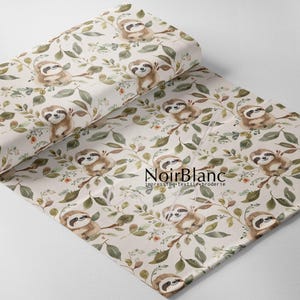 May include: A roll of fabric with a repeating pattern of sloths on branches with green leaves and orange flowers. The sloths are brown and white, set against a cream background. The fabric has the text "NoirBlanc" printed on it.