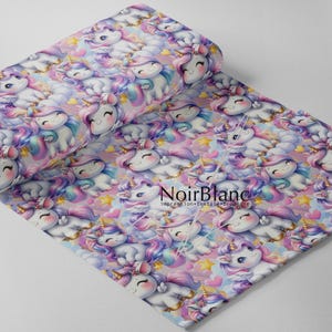 May include: A roll of fabric featuring a repeating pattern of smiling unicorns with rainbow manes and tails, set against a pastel sky with clouds, stars, and hearts. The fabric has the text "NoirBlanc" printed on it.
