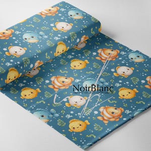 May include: A folded piece of blue fabric featuring a repeating pattern of cartoon fish in orange, yellow, and light blue, along with green seaweed and white bubbles. The text NoirBlanc impression textile broderie is printed in black.