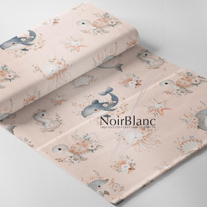 May include: A roll of fabric with a repeating pattern of marine life, including whales, turtles, jellyfish, and seahorses, in shades of blue, beige, and peach. The fabric has a soft, watercolor-like aesthetic, with floral accents. The text "NoirBlanc" is visible.