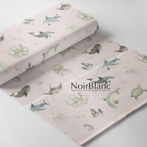 May include: Pink fabric with a repeating pattern of watercolor sea creatures, including dolphins, jellyfish, seahorses, starfish, and a whale. The text "NoirBlanc impression-textile-broderie" is printed in the bottom center of the fabric.