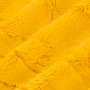 May include: Close-up of a soft, yellow faux fur fabric with a textured, wavy pattern.