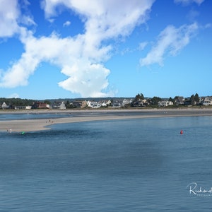 Könnte beinhalten: Panoramablick auf einen Sandstrand mit einer kleinen Insel in der Mitte einer Bucht. Der Strand ist von Häusern und Bäumen gesäumt. Der Himmel ist blau mit weißen Wolken.