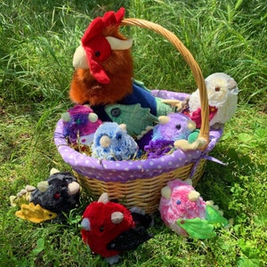 Pode incluir: Uma cesta de vime cheia de brinquedos de pel&uacute;cia coloridos, incluindo um galo, um drag&atilde;o e uma variedade de outras criaturas. A cesta &eacute; forrada com tecido roxo e tem bolinhas brancas.