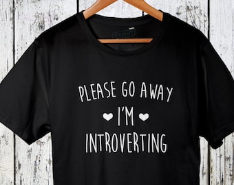 Pode incluir: Camiseta preta com texto branco que diz "Please go away I'm introverting" com dois pequenos corações brancos de cada lado da palavra "I'm".