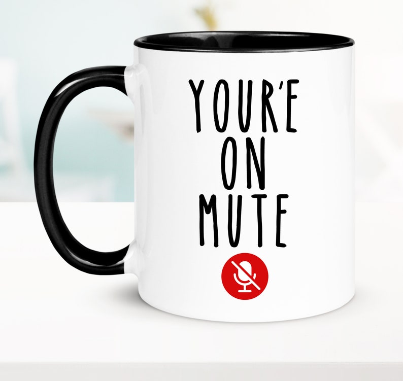 May include: White ceramic coffee mug with a black rim and handle. The mug has black text that reads "YOU'RE ON MUTE" with a red microphone icon with a diagonal line through it.