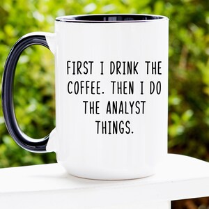 May include: White coffee mug with a black handle and black rim. The mug has the text "First I drink the coffee. Then I do the analyst things." printed on it.