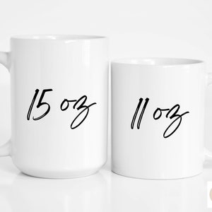 May include: Two white ceramic mugs with black handwritten text. The larger mug says "15 oz" and the smaller mug says "11 oz".