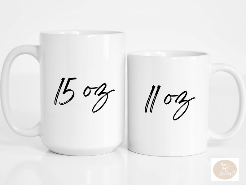 May include: Two white ceramic mugs with black handwritten text. The larger mug says "15 oz" and the smaller mug says "11 oz".