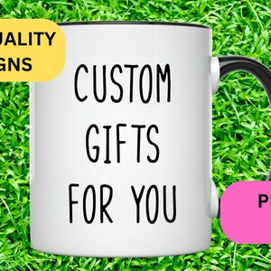 May include: White ceramic mug with a black handle and black rim. The mug has the text "CUSTOM GIFTS FOR YOU" printed on it. The mug is sitting on a green grassy surface. There is a yellow rectangle with the text "HIGH QUALITY DESIGNS" and a pink rectangle with the text "PERFECT GIFTS" on either side of the mug.