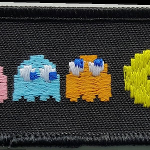 May include: Embroidered patch featuring the classic Pac-Man video game characters.  The patch shows Pac-Man chasing four ghosts: red, pink, blue, and orange.  The patch is black with colorful embroidery.