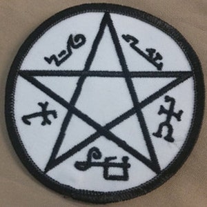 May include: A white, round patch with a black embroidered pentagram and five symbols around it. The symbols are: "Asmodeus", "Lilith", "Belial", "Lucifer", and "Samael".