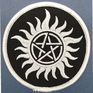 May include: White embroidered patch with a pentagram inside a circle with a sunburst design on a black background.