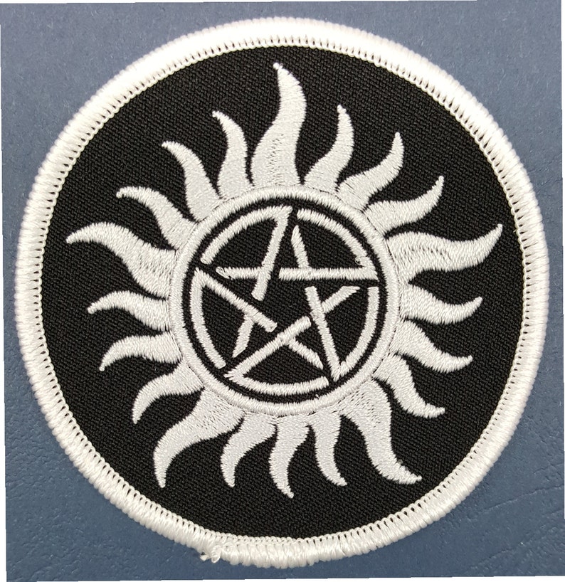 May include: White embroidered patch with a pentagram inside a circle with a sunburst design on a black background.