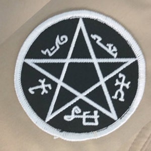 May include: Black and white embroidered patch with a five-pointed star and symbols around the perimeter. The star is filled in black and the symbols are white.