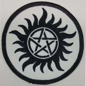May include: Black and white embroidered patch with a pentagram inside a circle of sun rays. The patch is circular and has a black border.