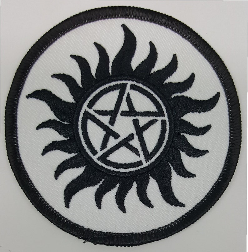 May include: Black and white embroidered patch with a pentagram inside a circle of sun rays. The patch is circular and has a black border.