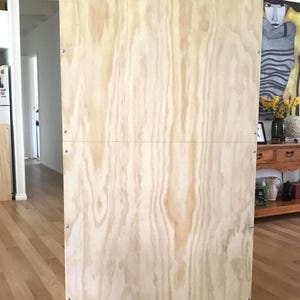 Puede incluir: Un tel&oacute;n de fondo de madera contrachapada de color marr&oacute;n claro con un marco y patas de madera. El tel&oacute;n de fondo est&aacute; de pie sobre un suelo de madera.