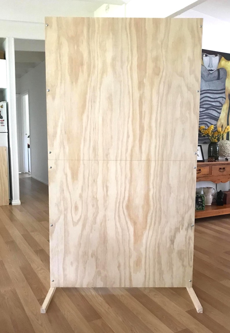 Puede incluir: Un tel&oacute;n de fondo de madera contrachapada de color marr&oacute;n claro con un marco y patas de madera. El tel&oacute;n de fondo est&aacute; de pie sobre un suelo de madera.