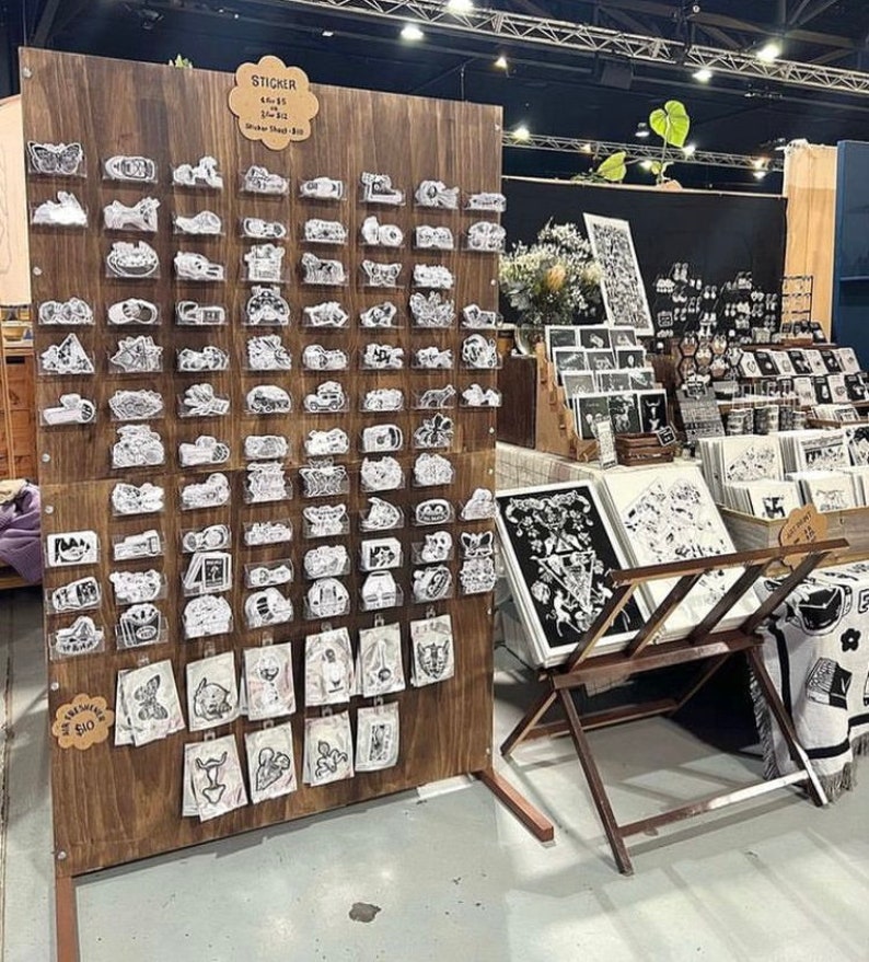 Puede incluir: Un tablero de madera con una variedad de pegatinas en blanco y negro a la venta. Las pegatinas est&aacute;n organizadas en filas y columnas en el tablero. El tablero est&aacute; etiquetado "Sticker Sheet 10 &euro;".