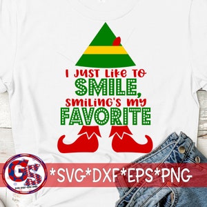 Op de afbeelding: Wit T-shirt met een groene elfenmuts en rode schoenen. De tekst op het shirt luidt "Ik hou er gewoon van om te lachen, lachen is mijn favoriet".