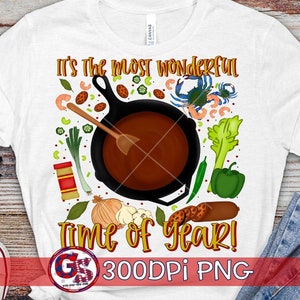 Könnte beinhalten: Weißes T-Shirt mit einer farbenfrohen Grafik, die eine gusseiserne Pfanne mit einem Holzlöffel zeigt, umgeben von Gemüse, Garnelen und einer Krabbe. Der Text lautet "It's the most wonderful Time of Year!"