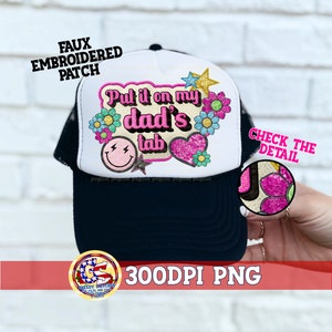 Pode incluir: Boné de caminhoneiro branco com aba preta. O boné tem um remendo bordado em rosa, amarelo e azul que diz "Put it on my dad's tab".