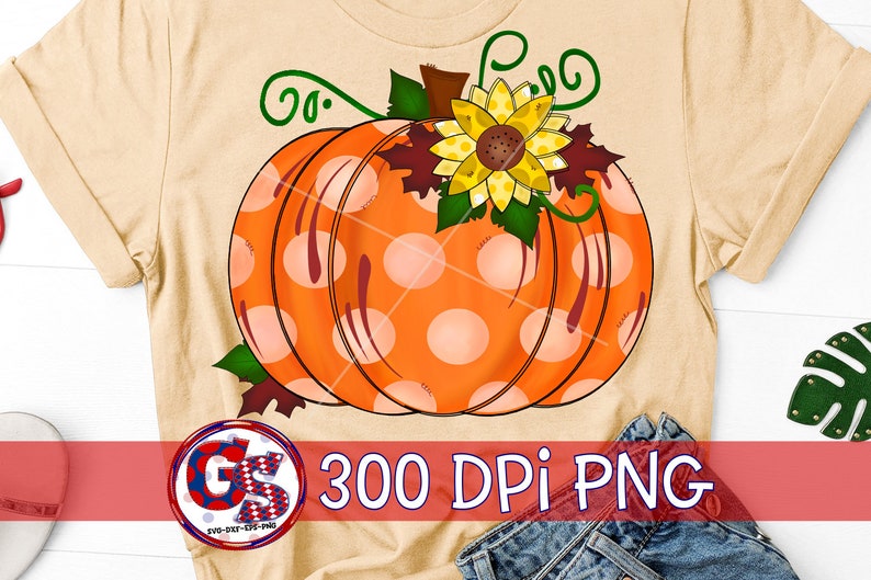 May include: A beige t-shirt featuring a large orange pumpkin with white polka dots, a yellow sunflower, and green vines. The text "300 DPI PNG" is displayed in the lower right corner. The design is perfect for fall and autumn-themed products.