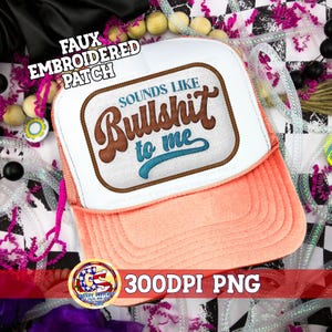 Puede incluir: Gorra de camionero con panel frontal blanco y visera y parte trasera de malla color melocotón. La gorra presenta un parche bordado con la frase "Sounds Like Bullshit to me" en letras marrones y turquesas.