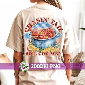 May include: Beige t-shirt with a graphic design featuring a pot of crawfish, corn, and the text "CHASIN' TAIL BOIL COMPANY". The design includes a blue and white checkered cloth and a watercolor style.