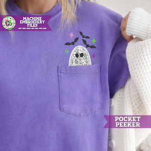 May include: A purple t-shirt with a chest pocket featuring an embroidered silver glitter ghost peeking out. Above the ghost are small black embroidered bats and colorful four-pointed stars. The text MACHINE EMBROIDERY FILES and POCKET PEEKER appear.