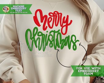 May include: Cream-colored sweatshirt with the words "Merry Christmas" in red and green script. The sweatshirt has long sleeves and a crew neck. The image also includes text that says "Machine Embroidery Files" and "For use with embroidery foam."