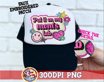 May include: White trucker hat with a black bill. The front of the hat has a pink and yellow embroidered patch that says "Put it on my mom's tab".