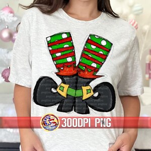 May include: A light grey t-shirt with a graphic of elf shoes. The shoes are black with green and red striped legs, green and gold buckles, and red accents. The text "300DPI PNG" is also visible on the shirt.