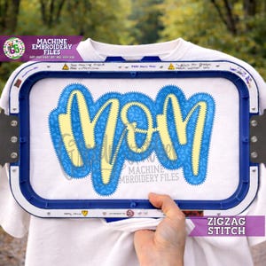 Puede incluir: Una camiseta blanca con un diseño "MOM" azul y amarillo, sujeta en un bastidor de bordado. El diseño presenta una puntada en zigzag. El texto en la imagen incluye "MACHINE EMBROIDERY FILES" y "ZIGZAG STITCH".