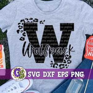 Puede incluir: Una camiseta gris con una letra negra "W" y el texto "Wolfpack" en una fuente de letra negra. La letra "W" está rodeada de manchas negras de estampado de leopardo. La camiseta está sobre una mesa con un dedo de espuma rojo con el texto "You're No. 1" en blanco.