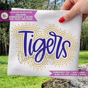 May include: A white fabric with the word "Tigers" in a blue script font, surrounded by gold-colored dots. The text "MACHINE EMBROIDERY & BLING SVG FILES INCLUDED" is also visible.