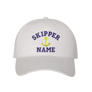 May include: White baseball cap with a navy blue embroidered anchor and the text "SKIPPER NAME" in navy blue.