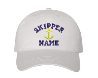 May include: White baseball cap with a navy blue embroidered anchor and the text "SKIPPER NAME" in navy blue.
