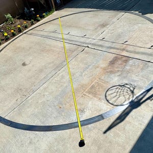 May include: A black circle painted on a concrete surface with a yellow measuring tape stretched across the diameter. The circle is approximately 15 feet in diameter.