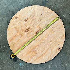 May include: A round piece of plywood with a yellow measuring tape across it. The tape measures 24 inches.
