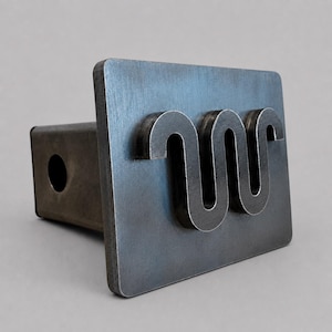 May include: A dark gray metal trailer hitch cover featuring a rectangular face plate with a raised, stylized, continuous wavy line symbol. The hitch cover has a square-shaped insert with a circular hole on the side for mounting purposes.
