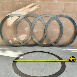 Puede incluir: Cuatro anillos de metal de diferentes tamaños, apilados uno encima del otro. Un quinto anillo de metal está acostado en el suelo con una cinta métrica amarilla a su lado.