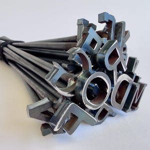 May include: A bundle of metal branding irons, each shaped as a letter of the alphabet. The irons are tied together with a black band. The letters are in a dark, metallic color, and the rods are silver.