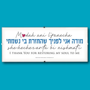 May include: A white sign with blue and black text that reads 'Modah ani l'panecha she hechezarta bi nishmati' which translates to 'I thank you for restoring my soul to me.' The sign also includes a small red heart.